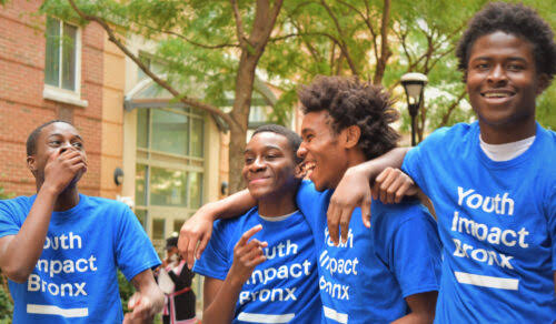 Four young people smiling together outdoors in Youth Impact Bronx shirts